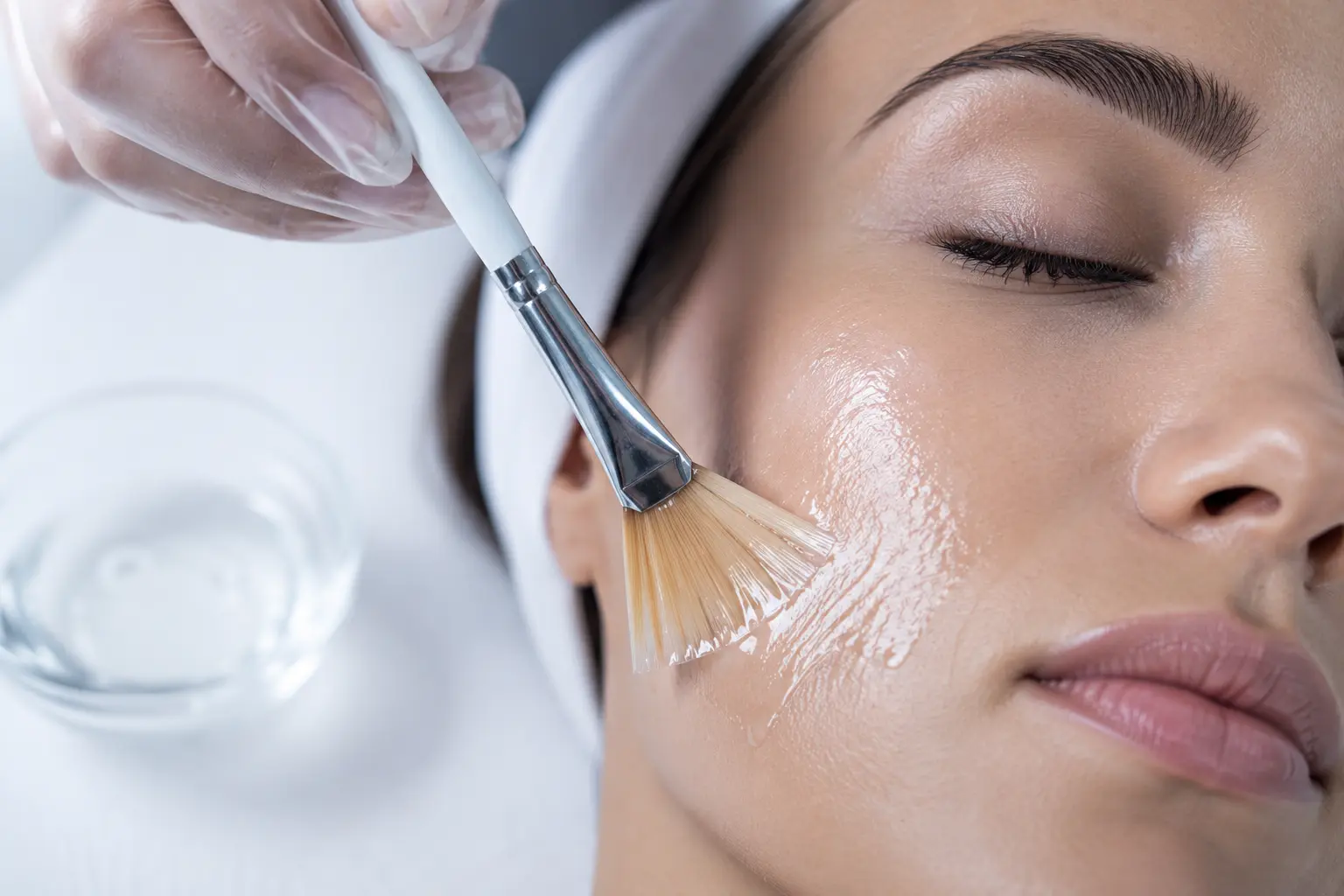 Advanced aesthetics educator carefully demonstrating a professional acid peeling application brush stroke onto a live model under clean clinical lighting.